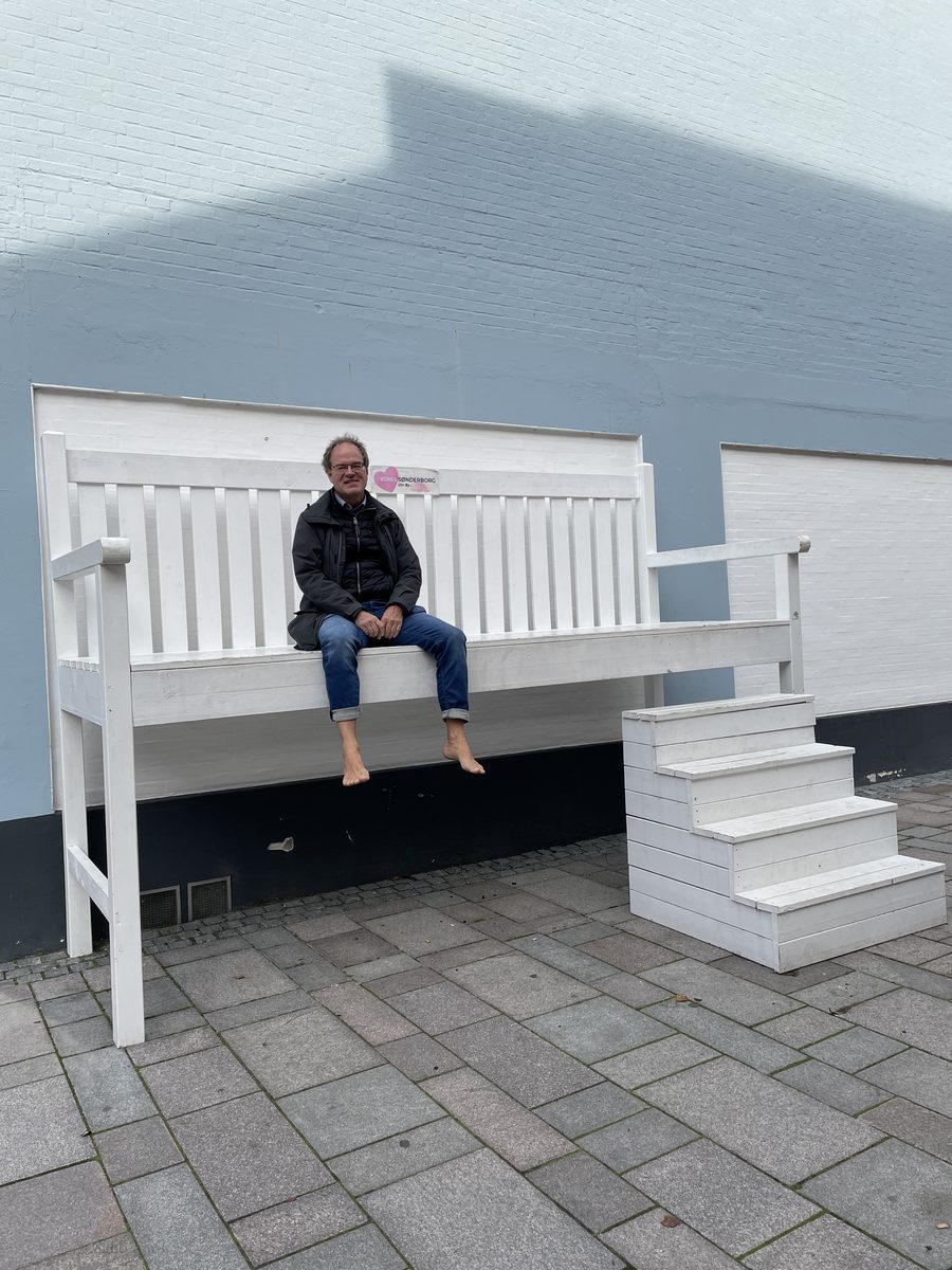 Nils sitzt barfuß auf einer überdimensionalen weißen Bank in Sønderborg